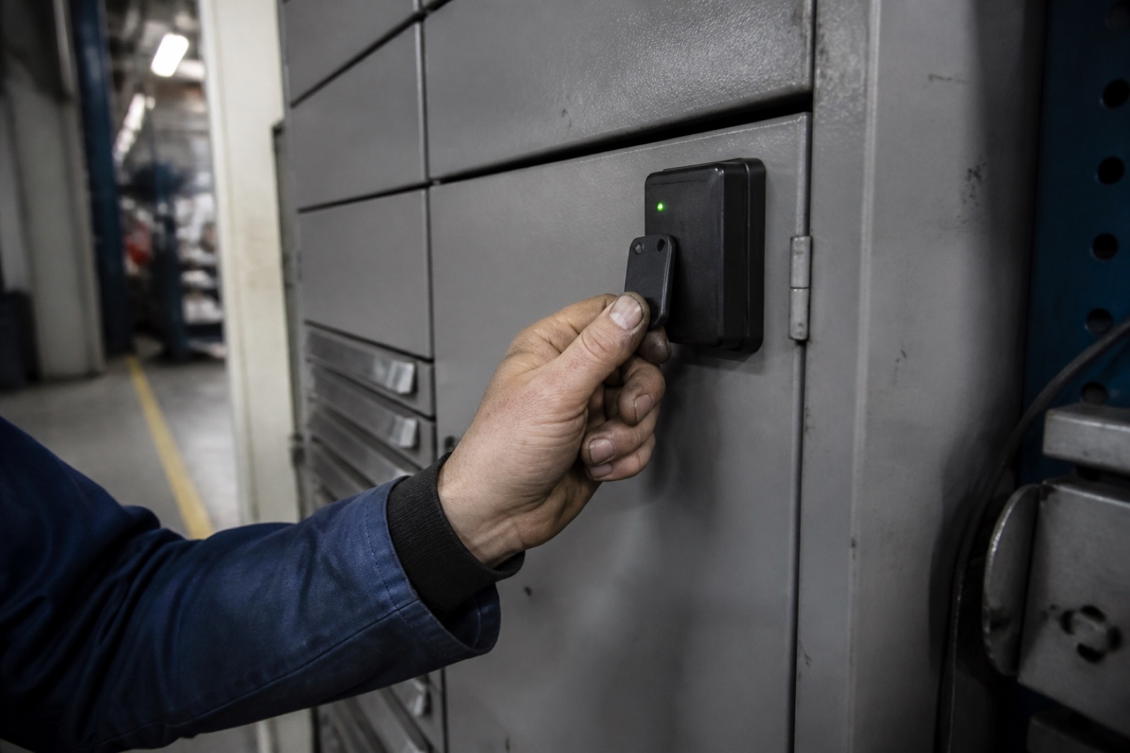 En hand håller upp en RFID-bricka mot en läsare på fronten av ett grått industriskåp.